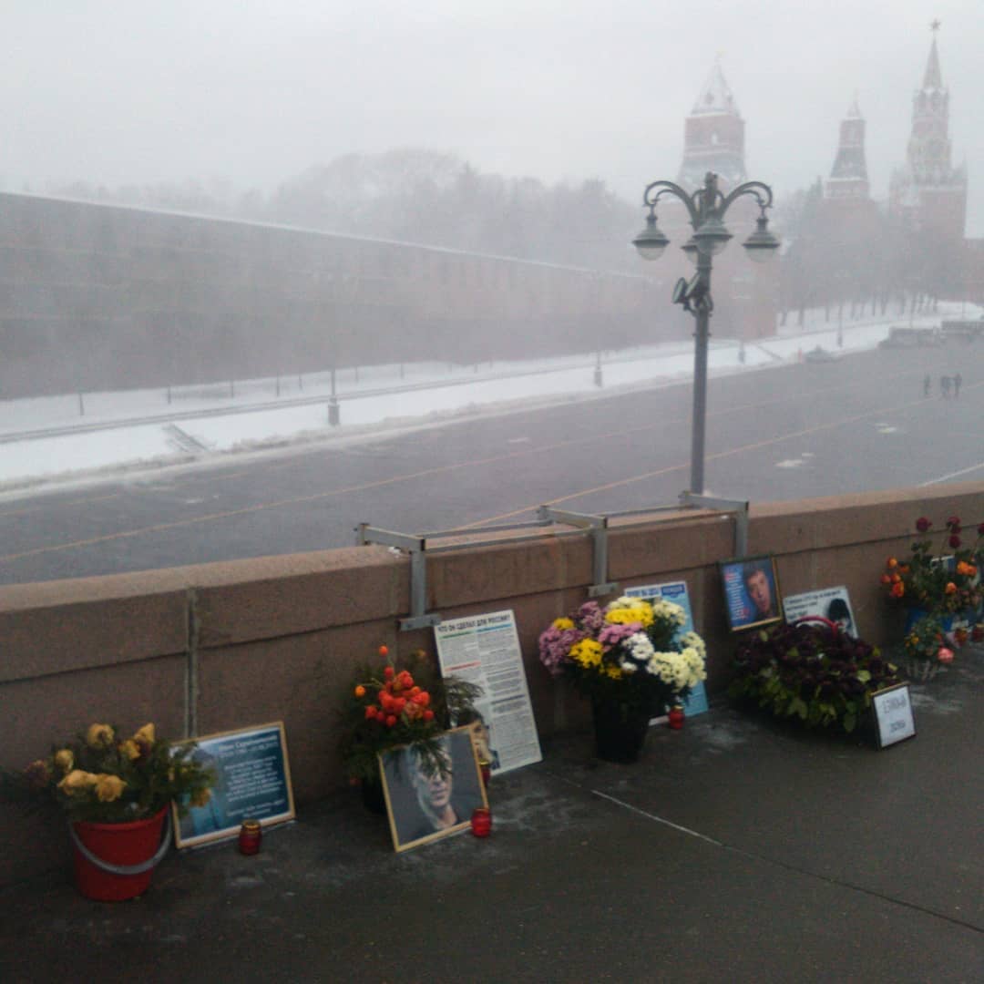 Мемориал на Немцовом (Большом москворецком) мосту на месте убийства Бориса Немцова.  Возле парапета моста стоят портреты Немцова, цветы и лампады.  На заднем плане через метель видны часть Васильевского спуска и три башни Кремля.